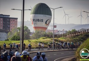 Ciclistas a pedalar no Granfondo Torres Vedras, com um balão de ar quente da Rubis Gás a flutuar ao fundo.