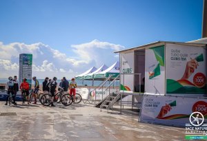 Ciclistas reunidos na marginal da praia num evento da Rubis Gás, junto a uma estrutura promocional do Clubis.