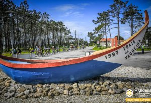 Pelotão de ciclistas da prova Aveiro Spring Classic a passar ao lado do monumento em forma de barco de arte xávega na Praia da Vagueira.
