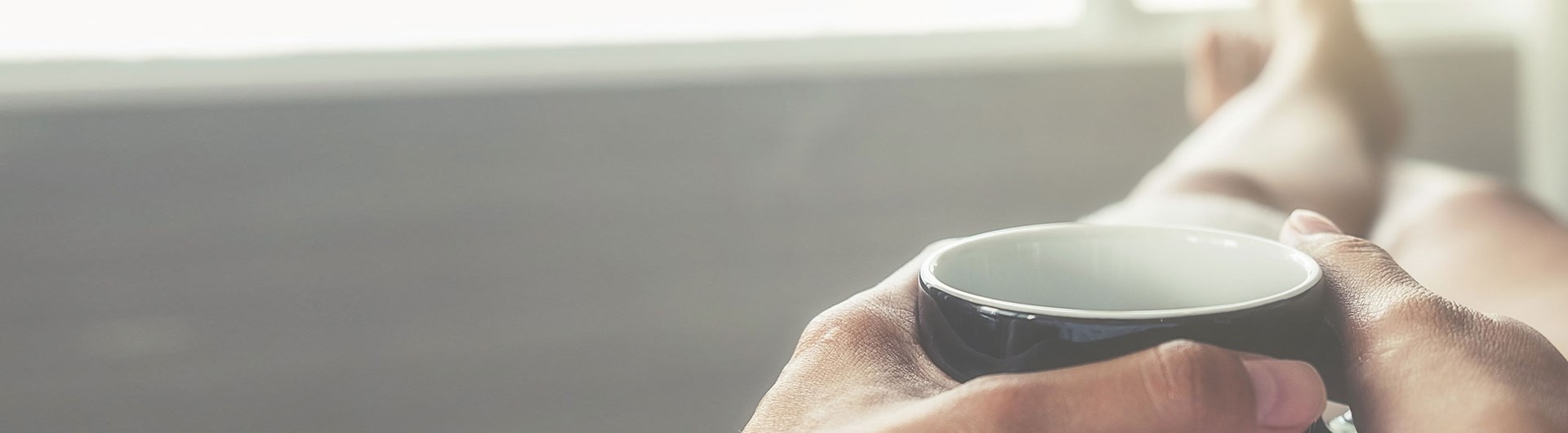 Pessoa a segurar uma chávena preta de café com as duas mãos