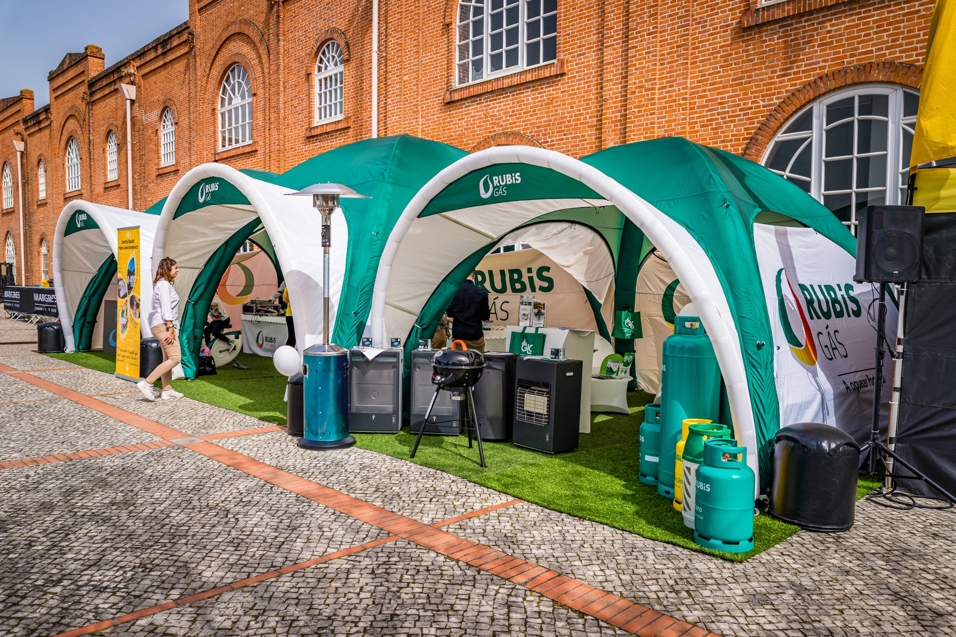 Stand promocional da Rubis Gás com tendas insufláveis verde e branco, exposição de aquecedores de exterior e garrafas de gás.