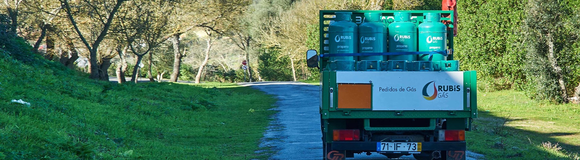 Traseira de um camião de distribuição carregado com garrafas de gás da Rubis Gás a circular numa estrada rural.