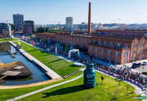 Vista aérea da concentração de participantes junto ao edifício de tijolo vermelho do Cais da Fonte Nova em Aveiro, com uma garrafa verde insuflável da Rubis Gás no relvado.